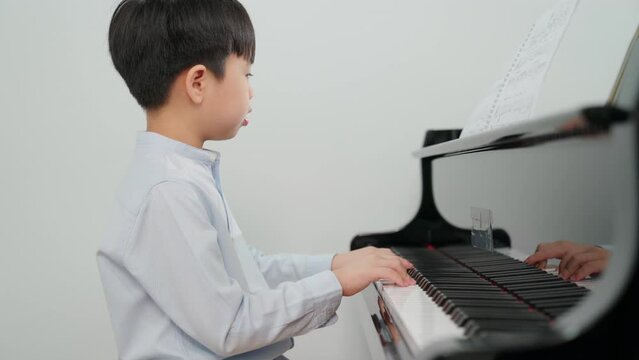 Side view of little boy learning or practice piano at school. Kid wearing casual shirt playing grand piano. Child having fun and happy to play music instrument. Education, skill and learning concept
