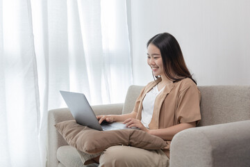 Naklejka premium Asian woman sitting on the sofa with a laptop, Looking at laptop screen, Relaxing at home, Working through the Internet communication system, Happy lifestyle, Feel good.