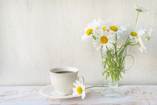 White cup of coffee and bouquet of white daisies on white paint wooden background; Summer morning still life;