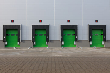 Row of loading docks with shutter doors at warehouse. Green gate, front view.