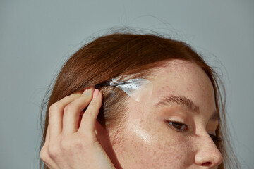 Fox eyes effect. Close up of redhead young girl using instant face lift band tape for slightly...