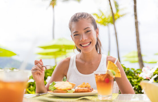 Happy Woman Eating Lunch At Outdoor Restaurant Terrace Plant Based Meat Burger With Pineapple. Hawaii Japanese Tropical Food. Asian Girl At Hotel Cafe Table During Summer Travel Vacation