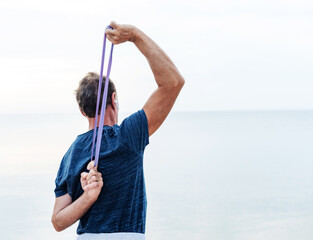 Active senior man is exercising outside with rubber band for sports. Sports equipment, gym concept,...