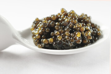 Natural black caviar in a white porcelain spoon on a white background. Product segment. Place for...