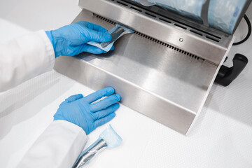 Close up view of dentist assistant's hands in latex gloves holding packaged with vacuum packing machine dental instruments ready for sterilizing in autoclave