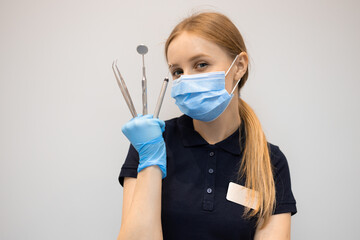 Portrait of a young woman dentist in a mask and latex gloves holding many dental instrument in hand. Dentistry concept