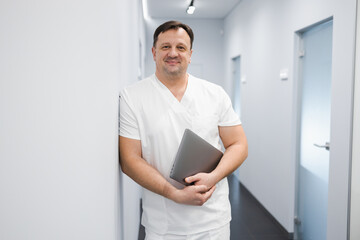 Portrait of a male surgeon with a laptop in the corridor in a hospital