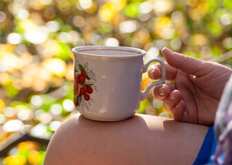In proud solitude, with a mug of tea, against the playful sunlight, among the yellow autumn leaves, brought out of sharpness.