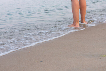 Man's bare feet stepping on calm seashore foamy wave and wet sand by evening, enjoying life and nature.