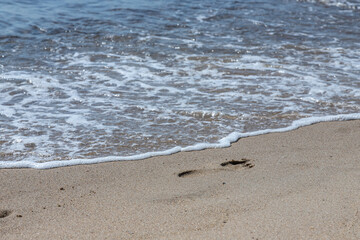 Footprints of a man on the yellow beach sand from walking barefoot by the sea with water that washes away the footprints.
