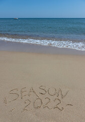 The inscription season 2022 on the sand by the water and the rising wave, seashore beach vacation by the sea
