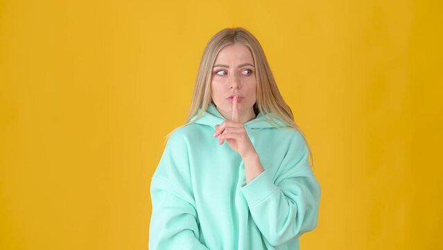 Women's secret. Young attractive blonde seriously showing silence gesture on camera isolated on yellow background