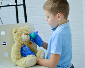 A boy in a blue T-shirt and medical gloves is playing doctor, washing the nose of a toy bear.