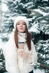 Portrait of woman drinking tea outdoors. Young woman with a cup of hot drink has fun in park in snowy weather.