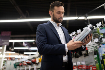 a man in a construction hypermarket chooses oil for a gasoline lawn mower