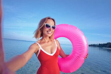 Technology and vacation. Pretty young woman in swimsuit taking selfie on the beach.
