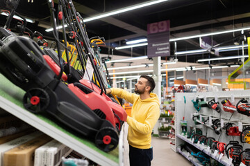 male buyer chooses a scarifier in a gardening equipment store