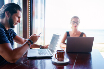 Coworking and freelance concept. Young  bearded man  and young woman working together on laptop...