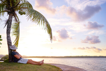 Tropical vacation. Young man resting under the palm tree.
