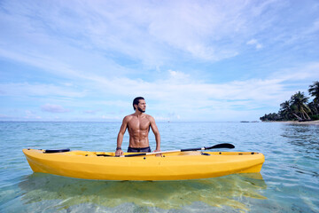 Young man with sea kayak on the tropical beach.