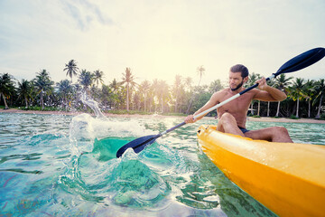 Young man paddling the sea kayak in the tropical calm lagoon.