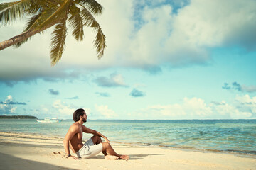Enjoying suntan and vacation.Young bearded man  ralaxing on the tropical sand beach.