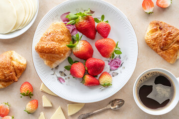 Fresh strawberries and sweet croissant on vintage plate over marble background.