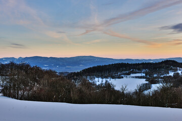 Winter snowy mountain landscape at dusk. Shortly after sunset. With forest and hills. Sky in blue oange. Nature background, wallpaper. Protected area Vrsatec, Slovakia.