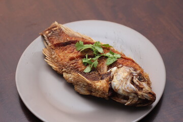 The fried tilapia was just right. Served in gray work on a brown wooden table.