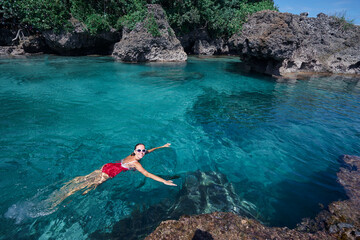 Summer vacation. Beautiful young woman in red swimsuit swimming at sea natural pool.