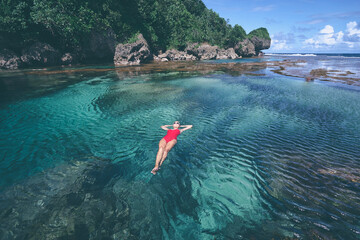Summer vacation. Young woman in red swimsuit bathing at sea natural pool.