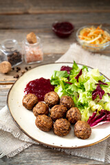 Swedish meatballs with salad and lingonberry jam in a bowl closeup. Traditional Scandinavian dish in a ceramic plate on a light gray wooden culinary background