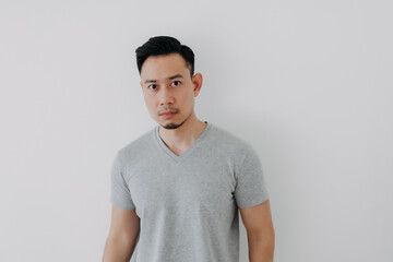 Straight face portrait of serious Asian man in grey t-shirt on white wall.