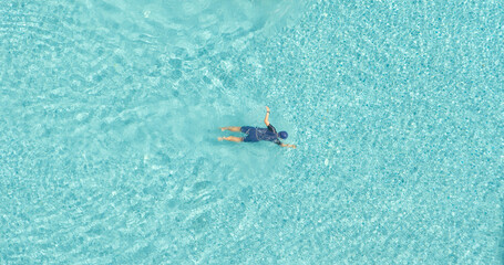 Aerial top view of a man swimming in blue or turquoise swimming pool with clear water ripple waves in summer season. People lifestyle on holiday vacation.