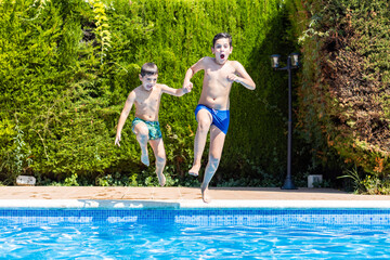 Two kids jumping into a pool in a sunny day