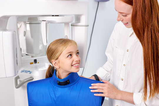 Professional Redhead Female dental specialist is going to examine an x-ray of child girl in modern dental clinic by professional specialist. little caucasian kid has dentist checkup. Portrait