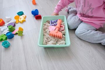 Light kinetic sand and figures. Hands of a little European girl. The child sculpts figures from bright details, animals. Educational game material for the early growth of the baby. Hand motor skills, 