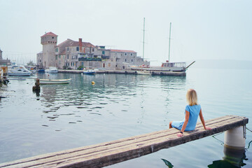 Tourism concept. Young traveling woman enjoying the view of Kastel Gomilica Castle sitting near the sea on Croatian coast.