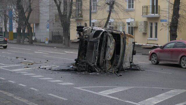 A burned-out police car lies on its side in the middle of the street after protests in Almaty city. Cars drive past burned-out military vehicle.