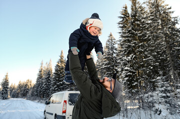 Fototapeta na wymiar a father with a beard and glasses holds his little son in his arms on a winter walk against the backdrop of a snowy forest