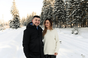 Young couple on the snow in winter in the park. love and vacation concept - happy couple hugging and laughing outdoors in winter