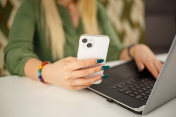 Freelancer woman using new white phone for online communication on lockdown. Entrepreneur person networking with smartphone app and laptop computer. Young female browsing social media news feed