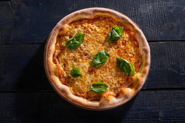 Cheese pizza decorated with basil isolated on dark wooden background top view