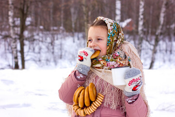 Cute girl in a traditional Russian headscarf with mug of hot tea and bagels on winter background.
