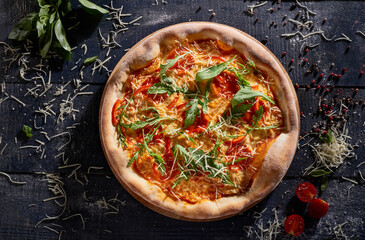 Pizza with tomatoes and arugula isolated on dark wooden background top view