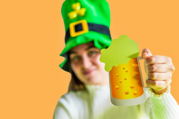 St. Patrick's Day leprechaun model girl in green hat and costume, holding mug of Beer pint over...