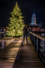 Fototapeta na wymiar A person takes a picture of a Christmas tree and the Deventer skyline at night