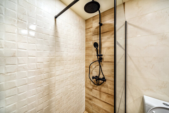 Modern shower zone with black rain head, hand held shower and glass door. Light beige and wood patern tiles in the bathroom.