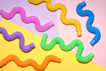Fototapeta premium Multi-colored corrugated plastic pipes on a bright background. Popular poptube game in the form of simple shapes and winding lines on a colorful background