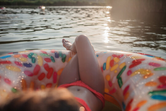 A smiling tween girl relaxing on a big donut shaped inflatable ring on a lake on a hot summer day, happy summertime in countryside, local vacations, cottagecore
